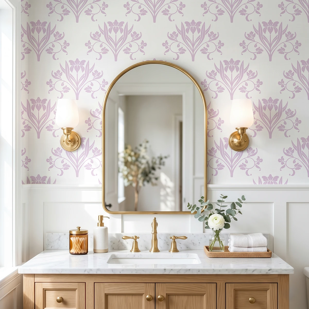 Liria, papel pintado floral lavanda y blanco, a escala grande en baño elegante con mueble de lavabo, espejo de arco y apliques de pared.