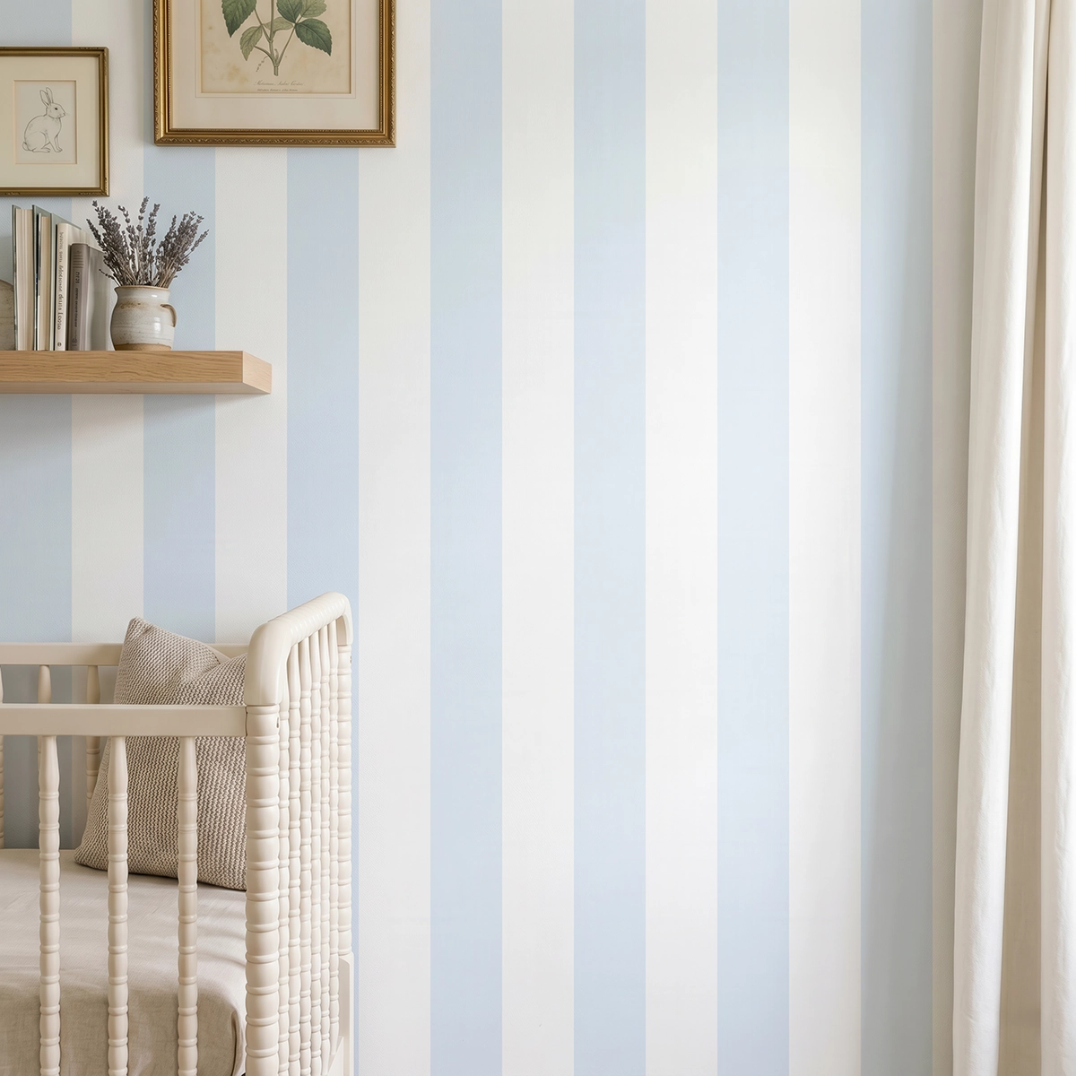 Modelo Della, papel pintado de rayas azul celeste y blanco, a escala grande en dormitorio infantil con cuna de bebé y pared decorada con una pequeña estantería con elementos decorativos.