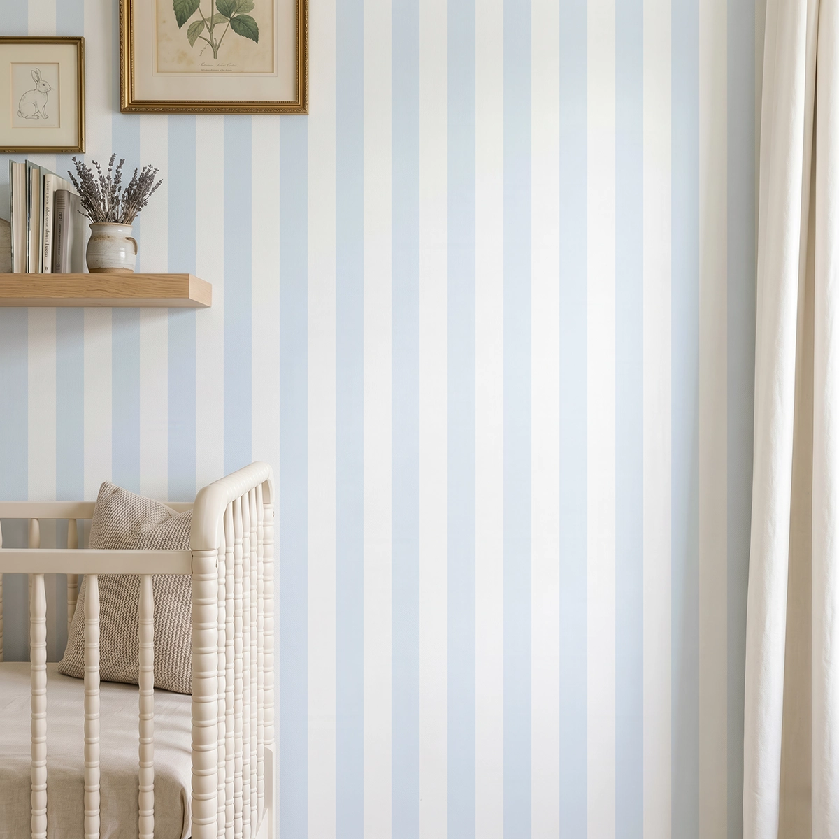 Modelo Della, papel pintado de rayas azul celeste y blanco, a escala mediana en dormitorio infantil con cuna de bebé y pared decorada con una pequeña estantería con elementos decorativos.