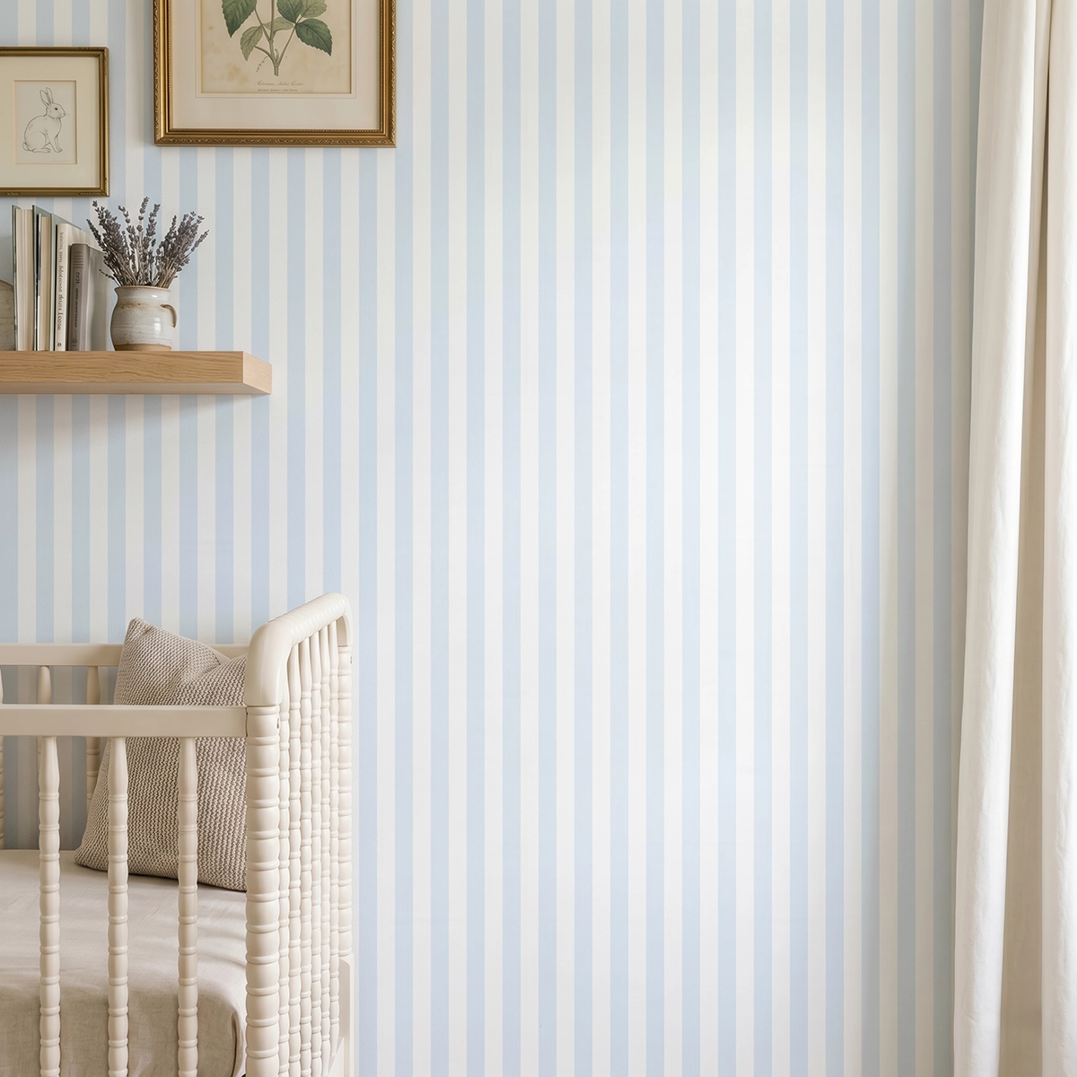 Modelo Della, papel pintado de rayas azul celeste y blanco, a escala pequeña en dormitorio infantil con cuna de bebé y pared decorada con una pequeña estantería con elementos decorativos.
