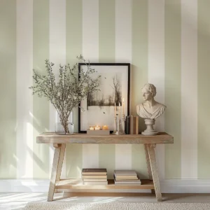 Modelo Della, papel pintado de rayas verde salvia y marfil, a escala maxi en pasillo o recibidor con consola de madera, decorada con un marco grande con una fotografía de un paisaje y otros elementos decorativos.