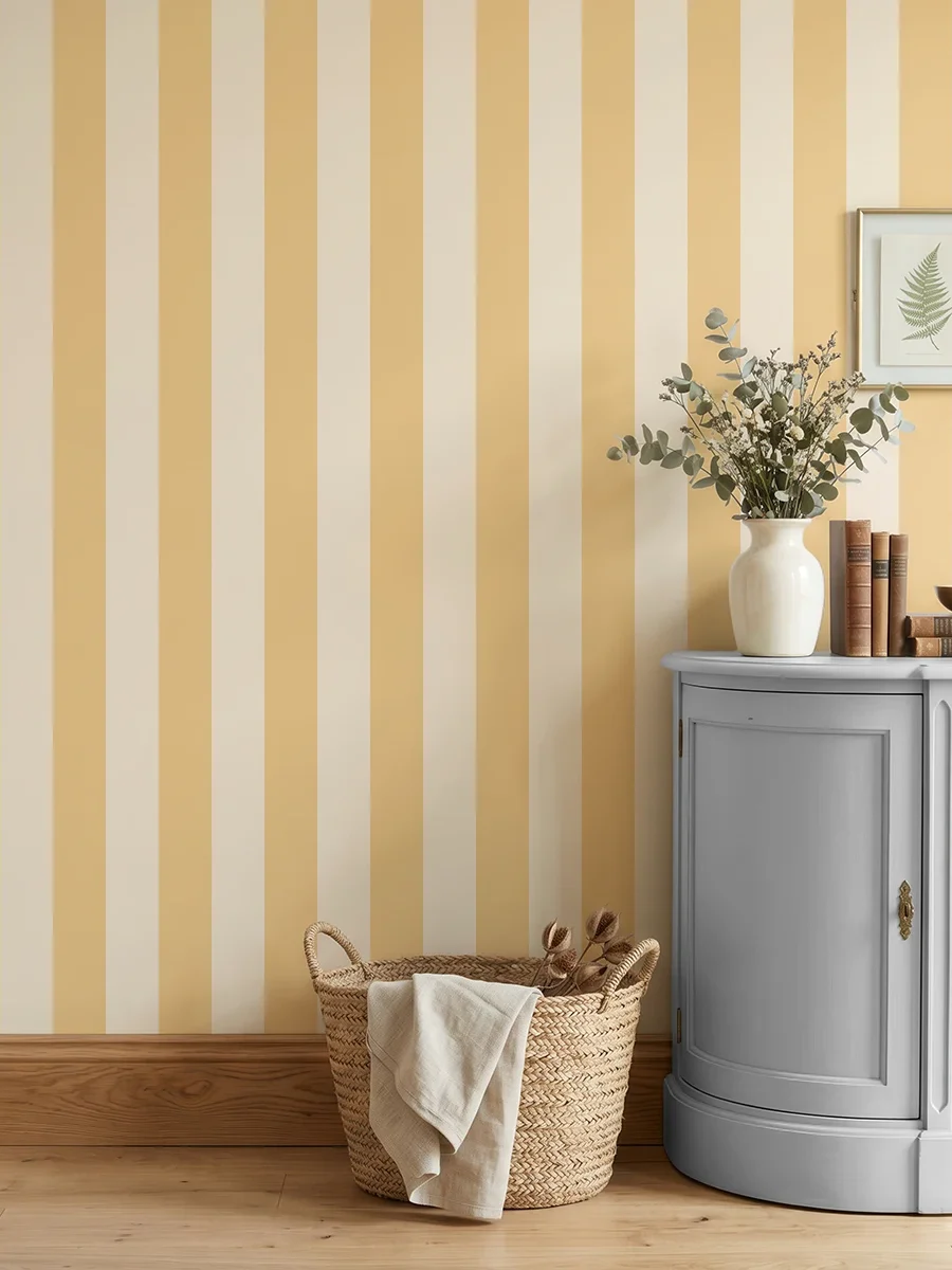 Modelo Della, papel pintado de rayas albaricoque y crema, a escala grande en cocina luminosa con mueble bajo de madera con jarrón con flores y con un cesto de esparto.