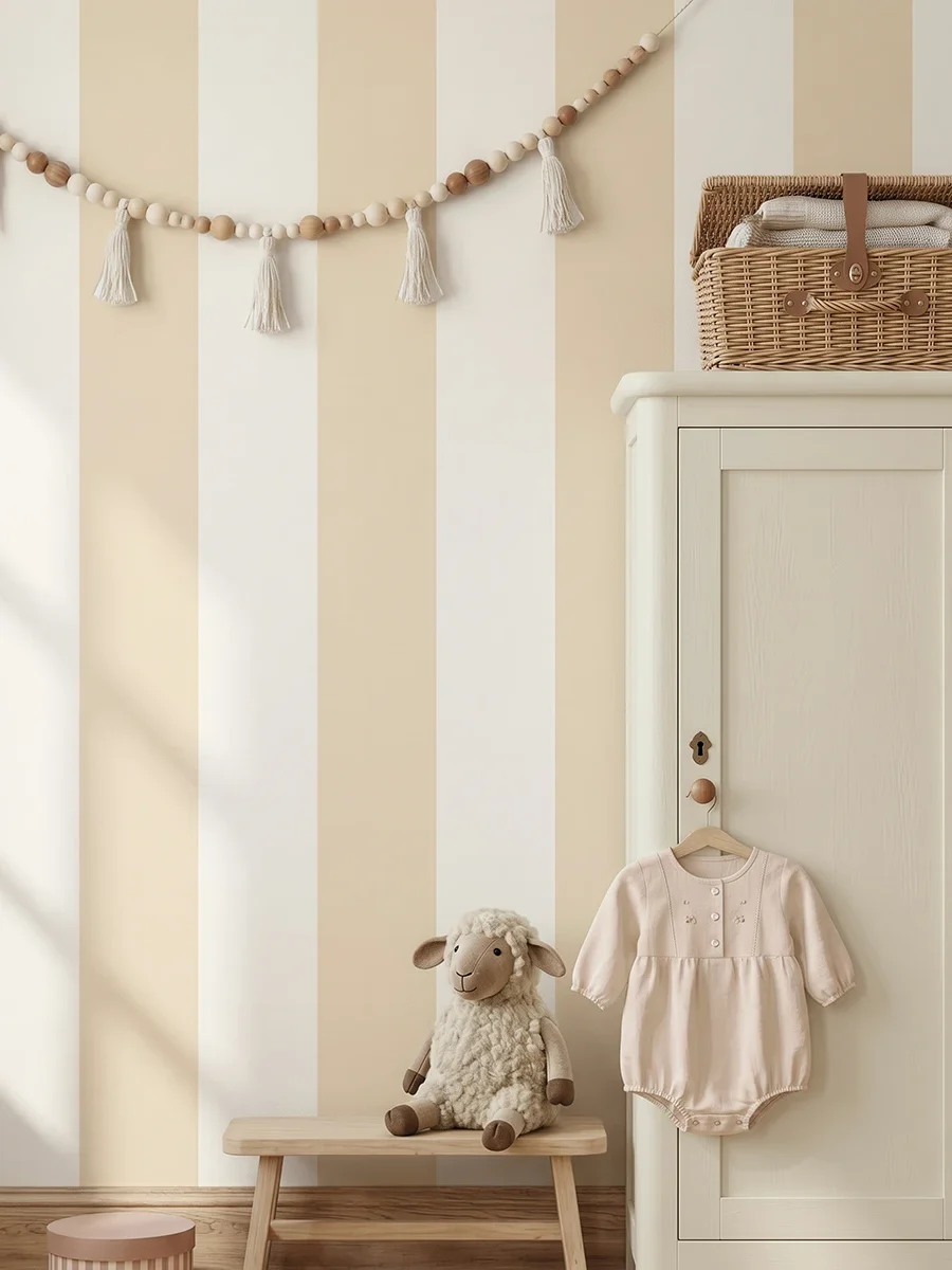 Modelo Della, papel pintado de rayas arena suave y marfil, a escala maxi en habitación infantil, con armario de madera con mameluco colgado y banco con peluche de oveja.