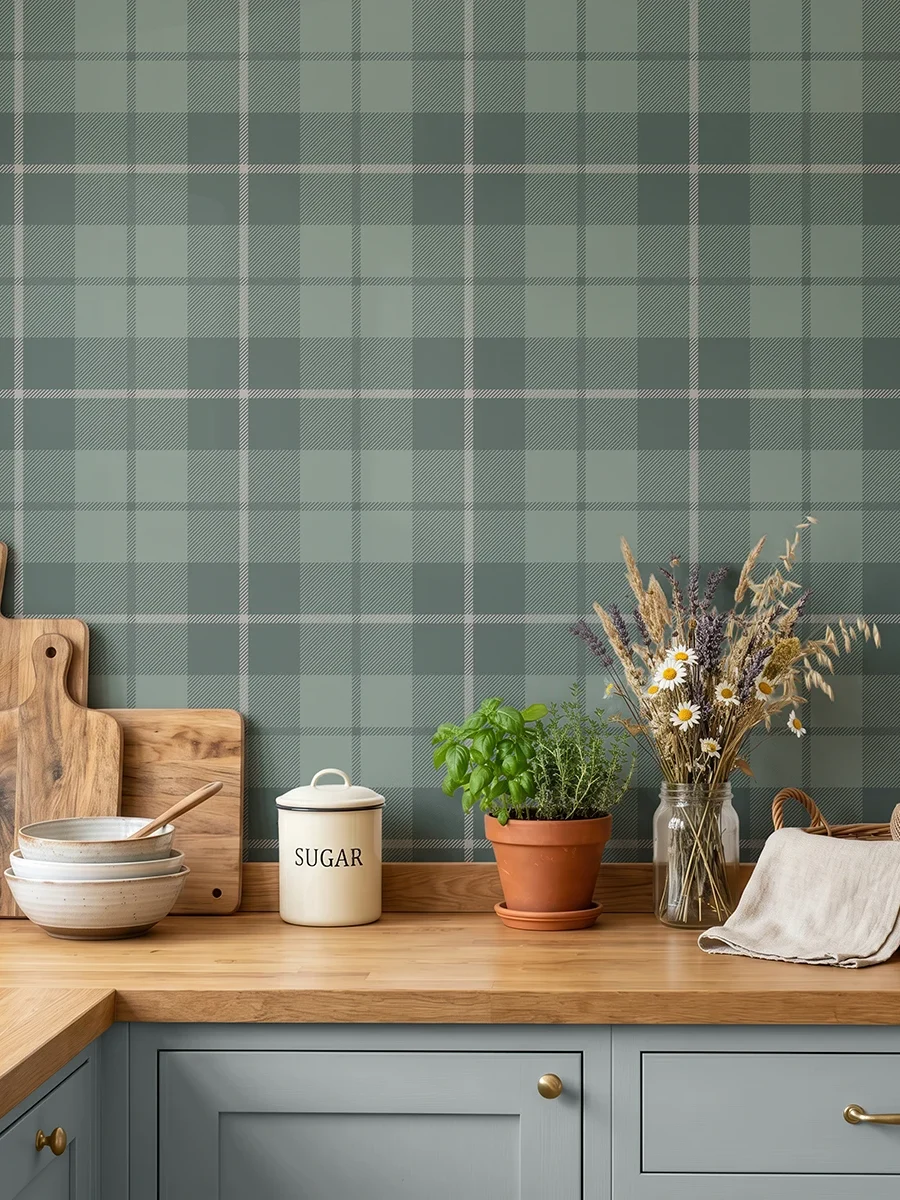 Modelo Oscar, papel pintado tartán verde bosque y gris, a escala mediana en cocina rústica con encimera de madera, sobre la cual aparecen utensilios de cocina y un tarro de cristal con flores silvestres..